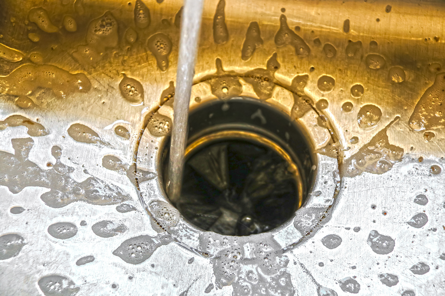 clean-garbage-disposal - Sam's Appliance Repair Water running into a garbage disposal of a stainless steel sink.