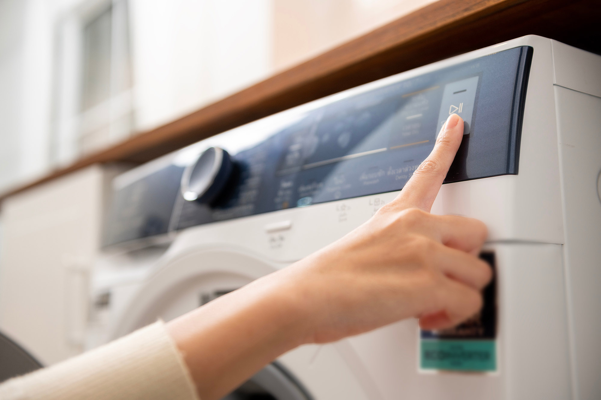 Close-up woman hand pushing washing machine buttons